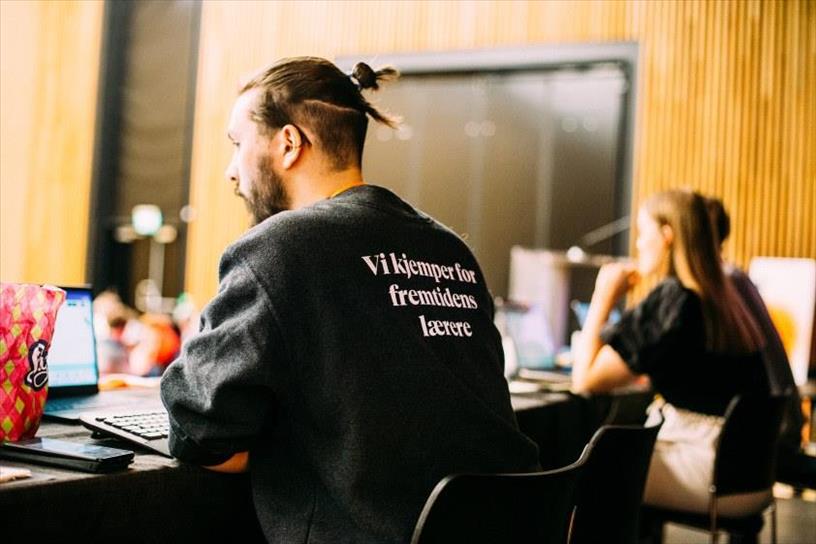 Bilde av en mann som sitter med ryggen til. På ryggen på genseren hans står det "vi kjemper for fremtidens lærere". Foto.